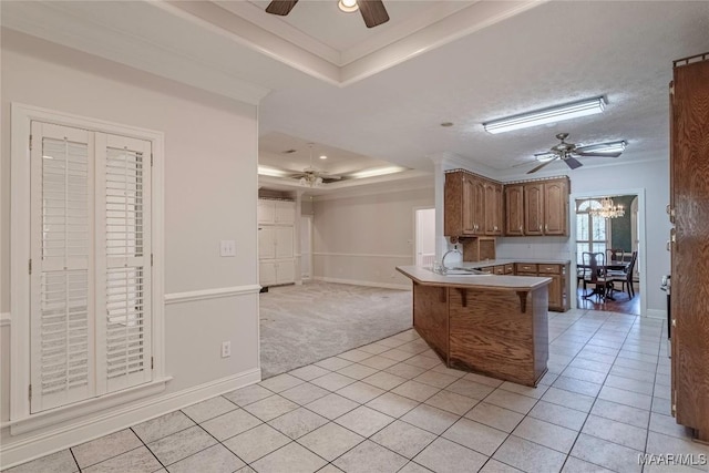 kitchen with a raised ceiling, a peninsula, and ceiling fan with notable chandelier