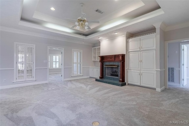 unfurnished living room featuring visible vents, light colored carpet, a premium fireplace, ornamental molding, and a tray ceiling