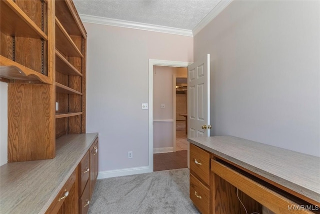 unfurnished office with crown molding, light colored carpet, built in study area, a textured ceiling, and baseboards