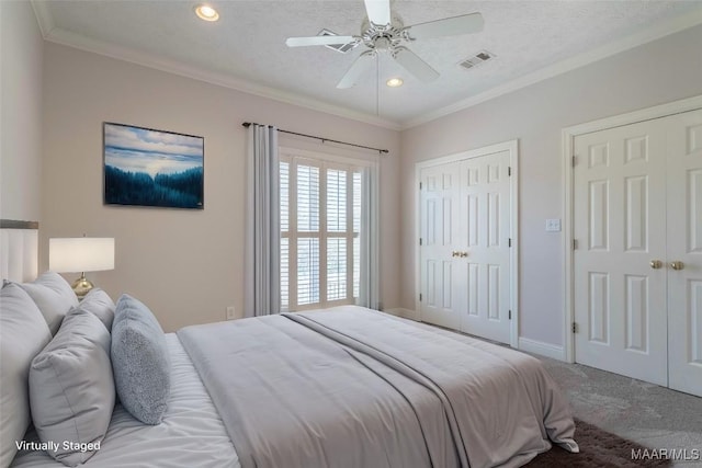 bedroom with two closets, crown molding, visible vents, and carpet flooring