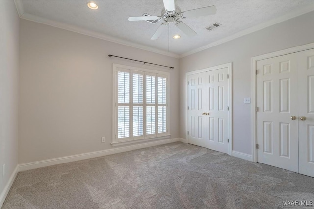 unfurnished bedroom featuring a textured ceiling, carpet floors, visible vents, baseboards, and crown molding