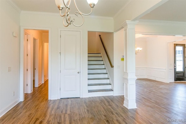 stairs featuring wood finished floors, crown molding, ornate columns, a chandelier, and a decorative wall