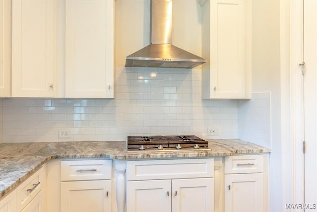 kitchen featuring tasteful backsplash, white cabinets, stainless steel gas cooktop, and wall chimney exhaust hood