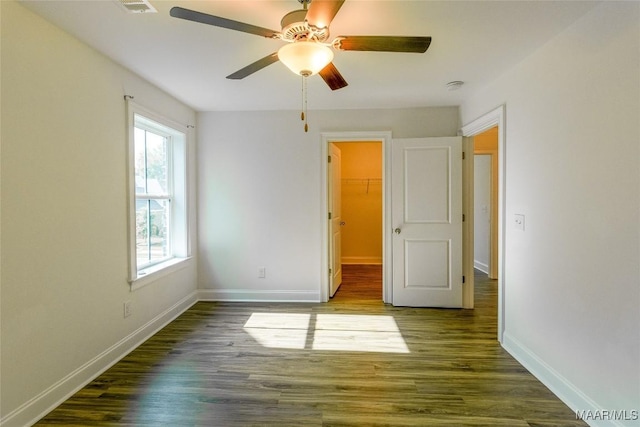 unfurnished bedroom featuring a walk in closet, a closet, a ceiling fan, wood finished floors, and baseboards