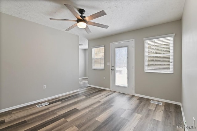 empty room featuring a healthy amount of sunlight, visible vents, and wood finished floors