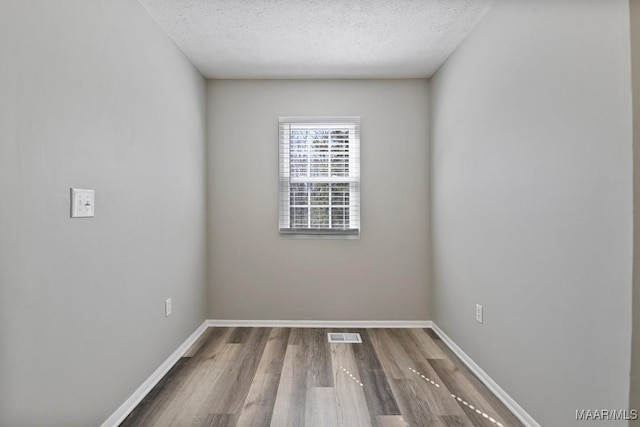 unfurnished room featuring visible vents, a textured ceiling, baseboards, and wood finished floors