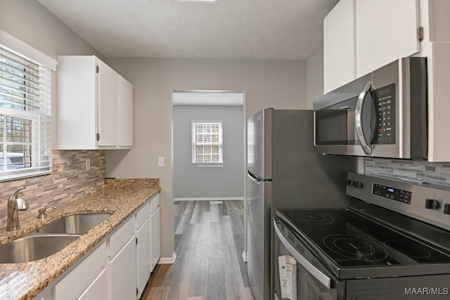 kitchen with light stone countertops, a sink, white cabinetry, appliances with stainless steel finishes, and decorative backsplash