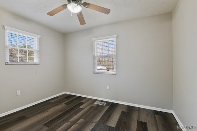 unfurnished room with dark wood-style flooring, visible vents, plenty of natural light, and baseboards