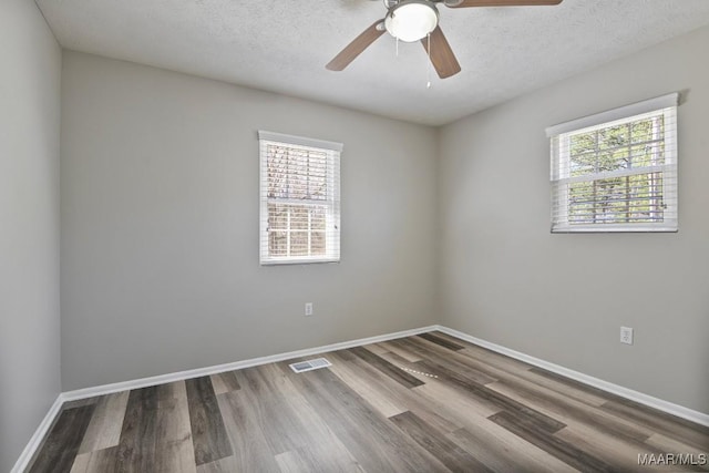 spare room featuring a healthy amount of sunlight, a textured ceiling, visible vents, and wood finished floors