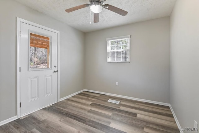 empty room with a textured ceiling, ceiling fan, wood finished floors, visible vents, and baseboards