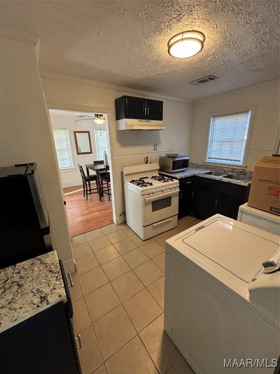 kitchen with under cabinet range hood, dark cabinetry, stainless steel microwave, and white range with gas stovetop