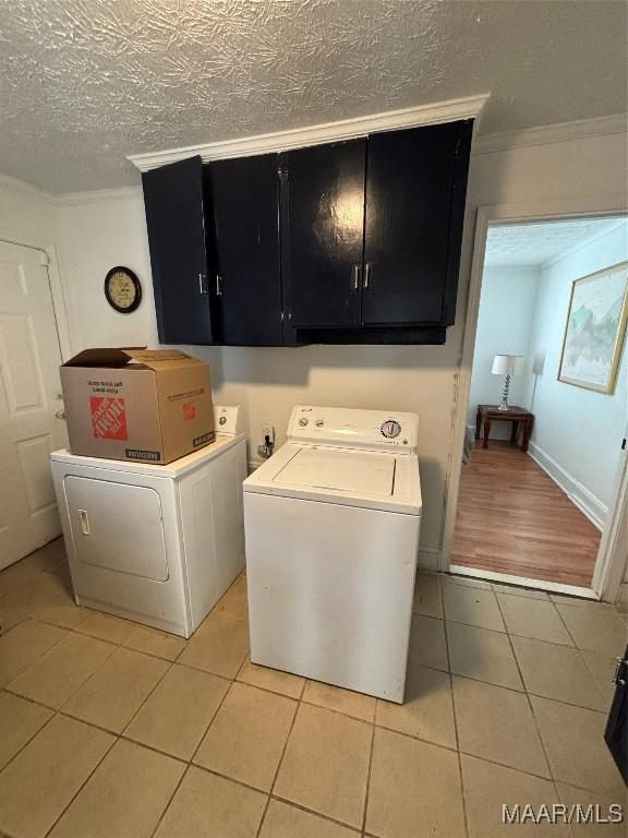 clothes washing area with light tile patterned floors, a textured ceiling, ornamental molding, cabinet space, and washer and clothes dryer