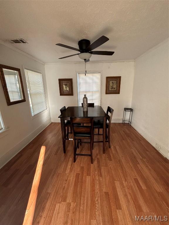 dining space with a textured ceiling, baseboards, wood finished floors, and crown molding