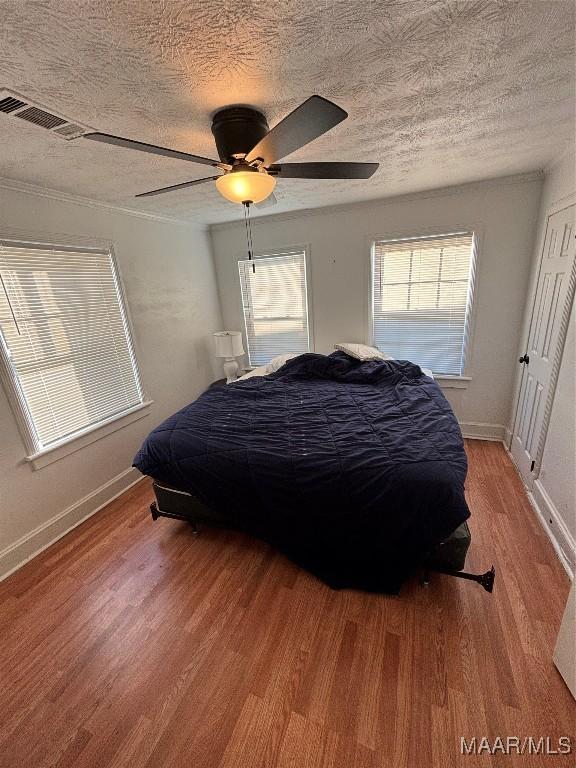 bedroom with visible vents, baseboards, a ceiling fan, a textured ceiling, and light wood-style floors