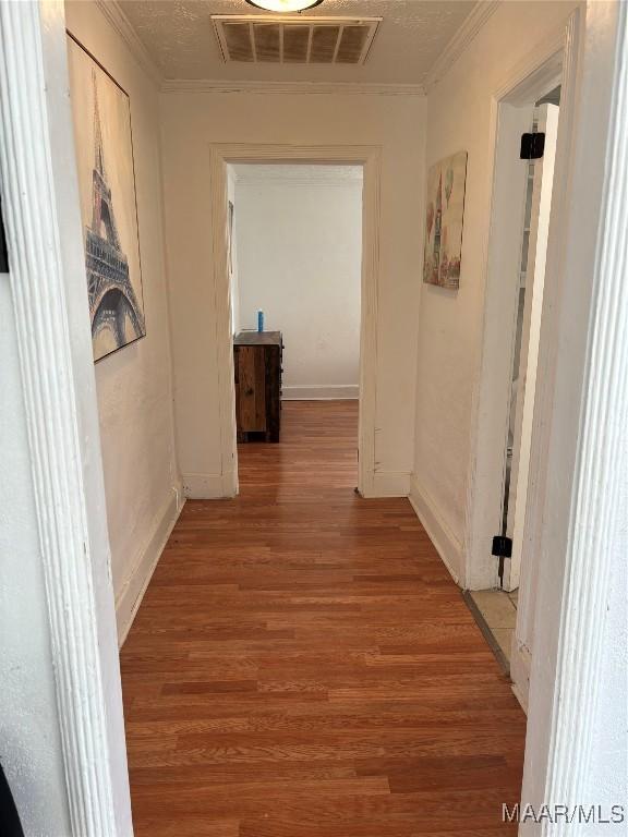 hallway featuring visible vents, crown molding, baseboards, and wood finished floors