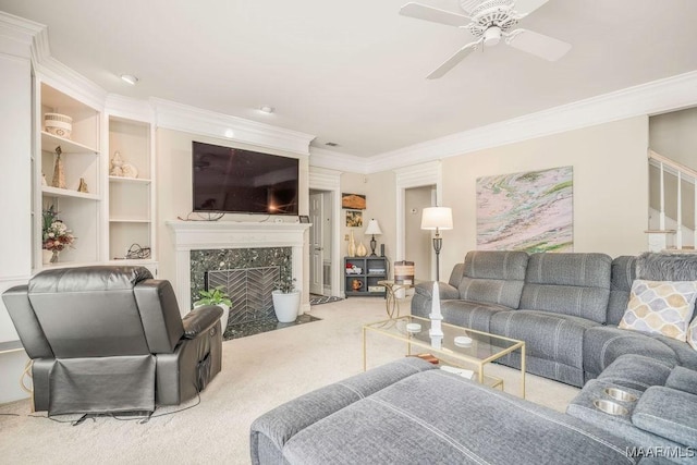 living area featuring carpet, a premium fireplace, ornamental molding, a ceiling fan, and stairs