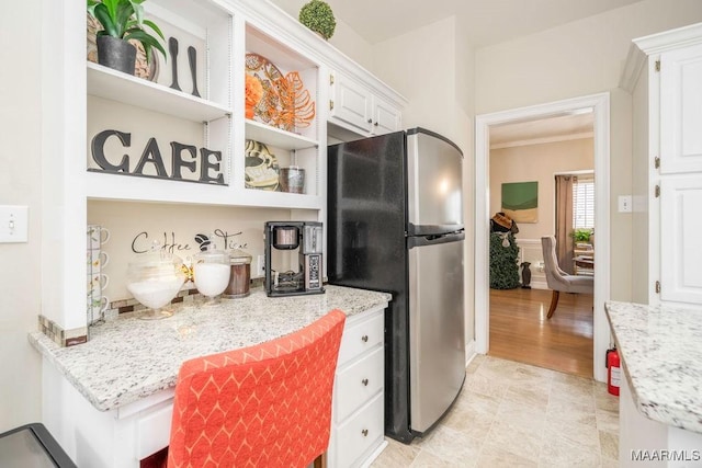 kitchen featuring crown molding, light stone counters, freestanding refrigerator, and white cabinetry