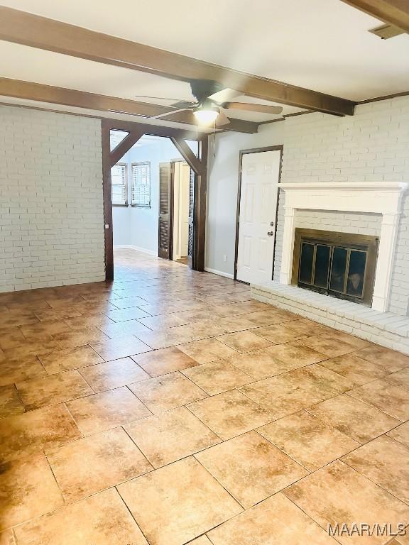 unfurnished living room with a fireplace, a ceiling fan, brick wall, beamed ceiling, and baseboards