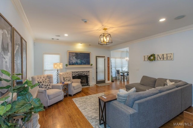 living area with a tile fireplace, recessed lighting, a notable chandelier, wood finished floors, and crown molding