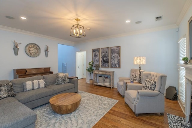 living room featuring crown molding, a fireplace, a notable chandelier, light wood finished floors, and visible vents