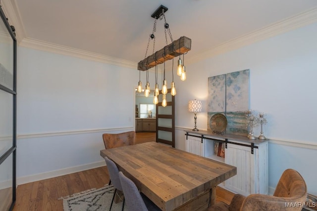 dining area featuring ornamental molding, a barn door, baseboards, and wood finished floors