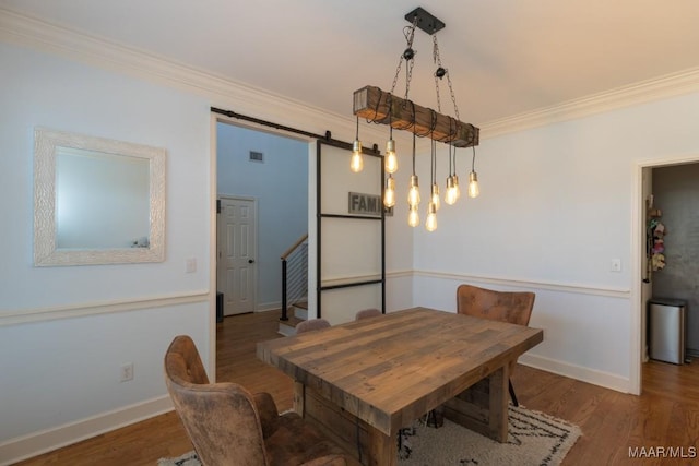 dining area with baseboards, a barn door, wood finished floors, and crown molding