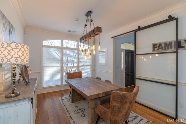 dining space featuring a barn door, visible vents, ornamental molding, and wood finished floors