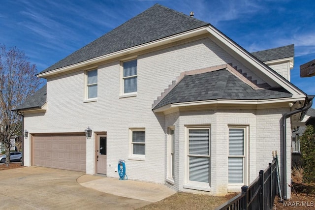 back of house featuring a garage, driveway, brick siding, and roof with shingles