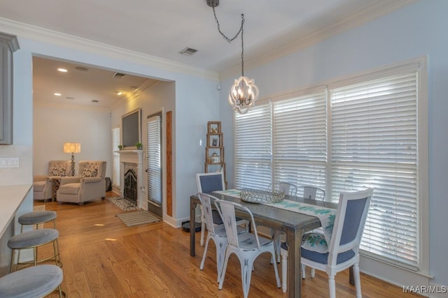 dining space with a notable chandelier, a fireplace, visible vents, light wood-type flooring, and crown molding