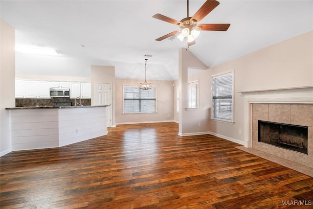 unfurnished living room featuring baseboards, a tile fireplace, dark wood-style floors, vaulted ceiling, and ceiling fan with notable chandelier