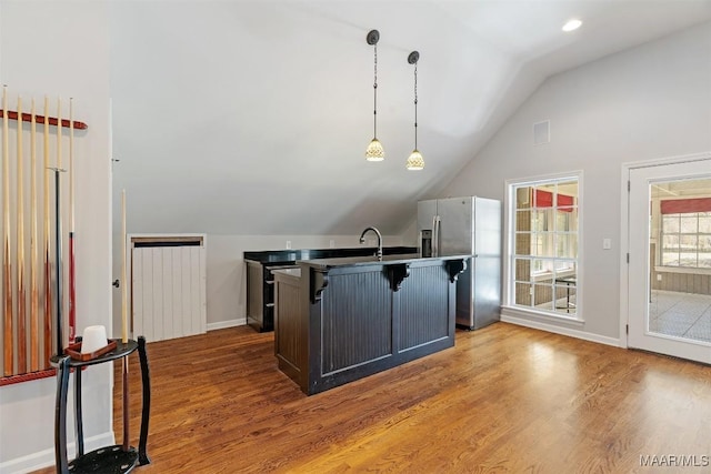 kitchen with pendant lighting, a breakfast bar area, lofted ceiling, wood finished floors, and stainless steel fridge