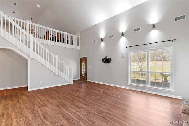 unfurnished living room featuring stairs, a high ceiling, wood finished floors, and visible vents