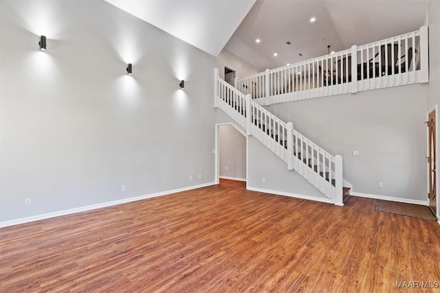 unfurnished living room featuring recessed lighting, a towering ceiling, stairway, wood finished floors, and baseboards