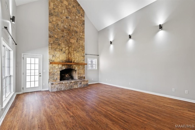 unfurnished living room with high vaulted ceiling, a stone fireplace, dark wood-style flooring, and baseboards