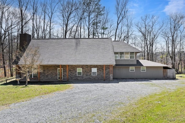 view of front of house featuring driveway, a chimney, stone siding, and a front yard