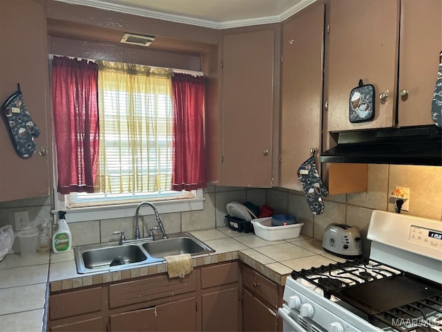 kitchen with white gas stove, under cabinet range hood, a sink, and tile countertops