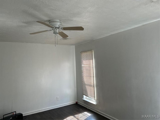 empty room with a textured ceiling, dark wood finished floors, visible vents, and baseboards