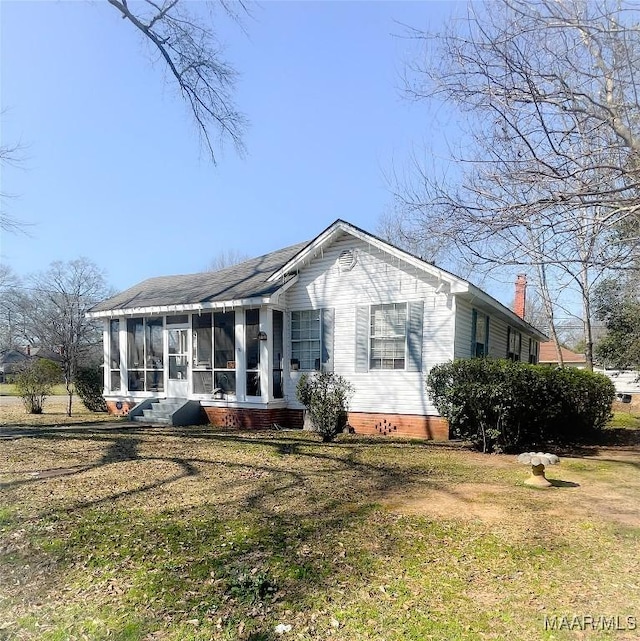 view of front facade featuring a front lawn, a chimney, and a sunroom