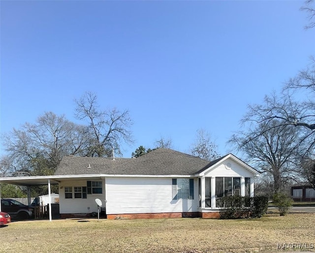 view of front facade with a carport, a sunroom, roof with shingles, and a front lawn