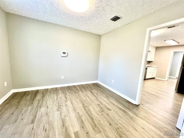 empty room featuring visible vents, light wood-style flooring, baseboards, and a textured ceiling