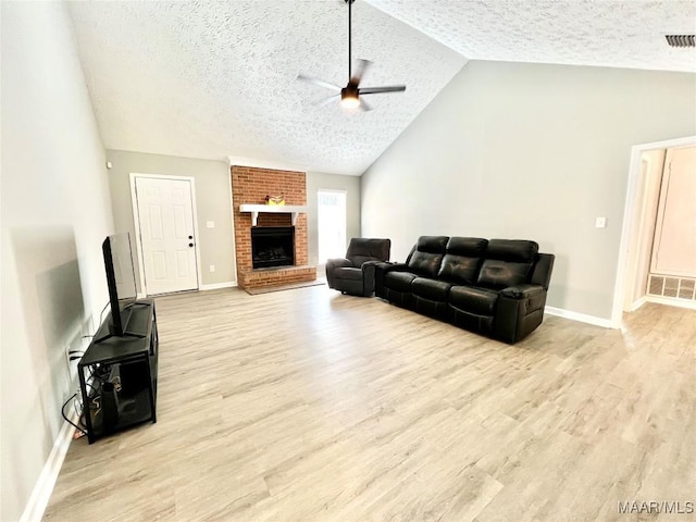 living area with lofted ceiling, light wood-style floors, a brick fireplace, ceiling fan, and a textured ceiling