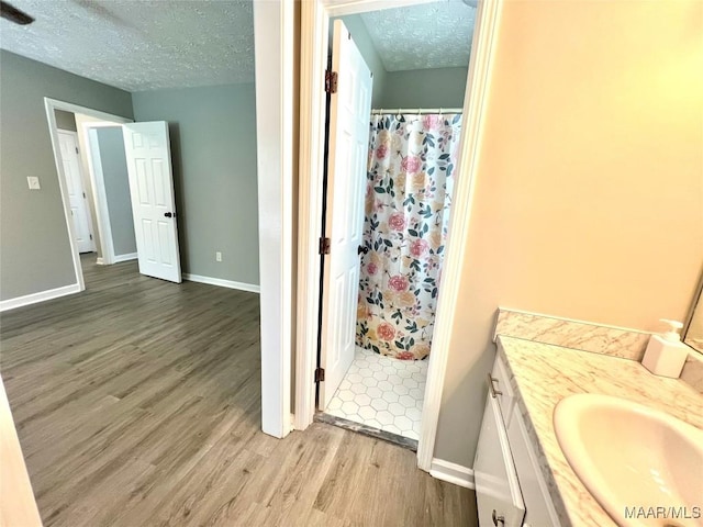 bathroom with baseboards, wood finished floors, curtained shower, a textured ceiling, and vanity