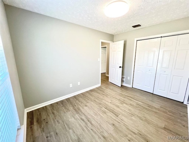 unfurnished bedroom with a closet, a textured ceiling, baseboards, and wood finished floors