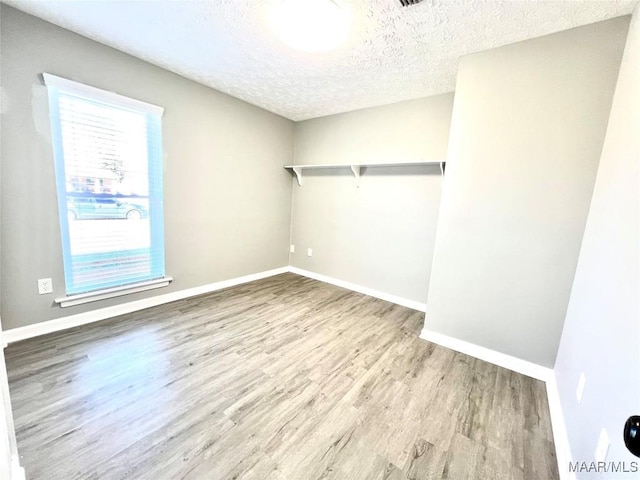 empty room featuring a textured ceiling, wood finished floors, and baseboards