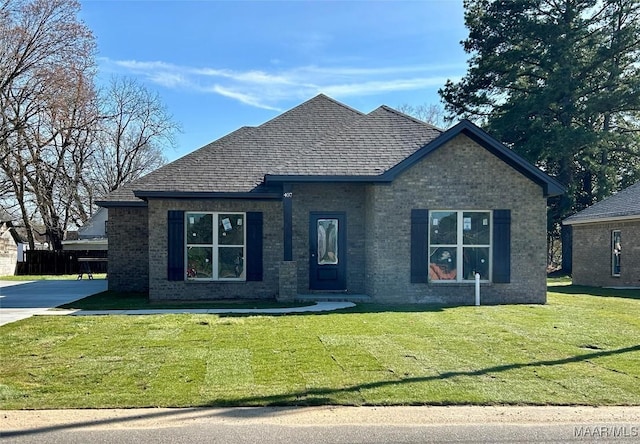 view of front facade with roof with shingles, a front lawn, and brick siding