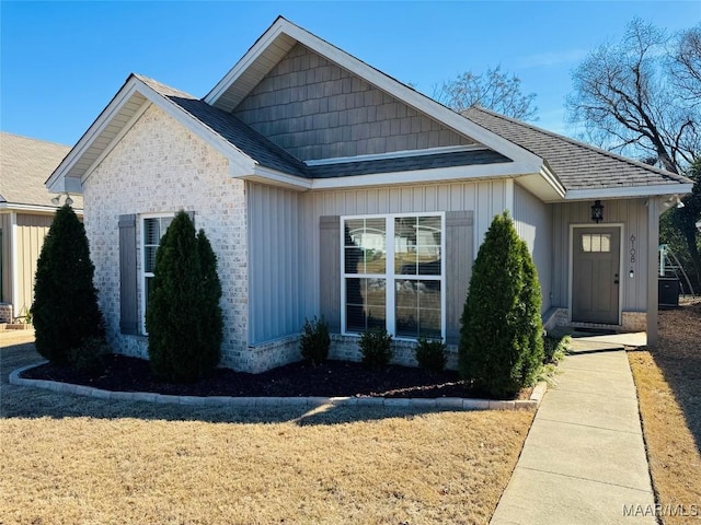 view of front of home featuring a shingled roof, brick siding, and a front lawn