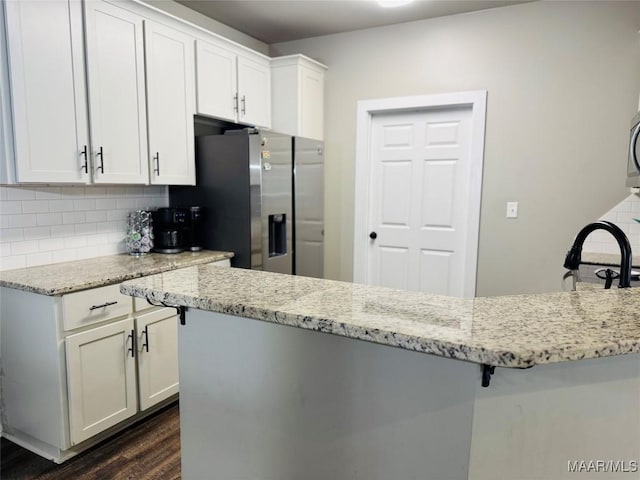 kitchen with white cabinetry, stainless steel refrigerator with ice dispenser, decorative backsplash, and light stone countertops