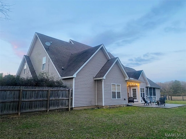 rear view of house featuring roof with shingles, a lawn, a patio area, and fence