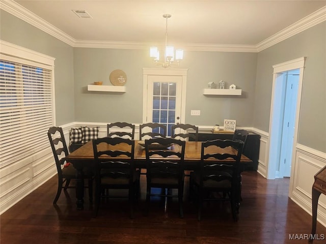 dining space with a wainscoted wall, a notable chandelier, visible vents, ornamental molding, and wood finished floors