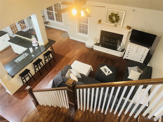 living area featuring a fireplace with raised hearth, wood finished floors, and a ceiling fan